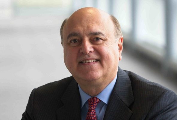 Headshot of Ed Pettinella inside near windows wearing a gray suit, blue shirt and orange tie